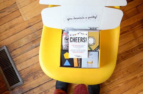 Work Anniversary Gift Box on a yellow chair filled with games, ice mold, confetti and cheers card