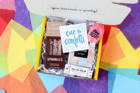 Small gift box on colorful backgrounf open and filled with Sprinkle Pretzels, confetti, balloon and lip balm: New Hire Gift Idea