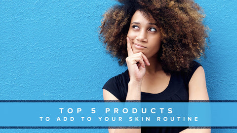 Diverse woman with curly hair leaning against a wall pondening which 5 skincare products to add to her routine