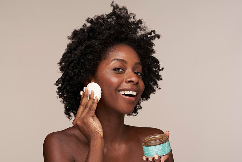 African American woman smiling while using the Even Tone Cleansing Bar and accompanying sponge
