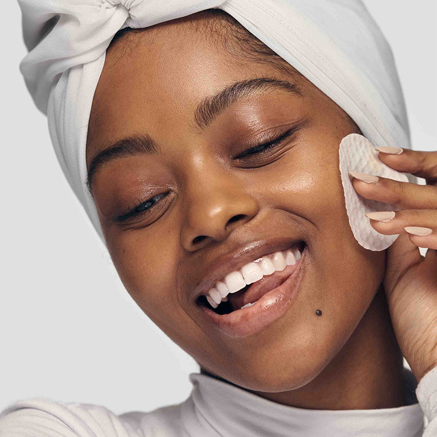 Diverse woman of deeper melenated skin tone, wiping her face with a textured round cotton pad