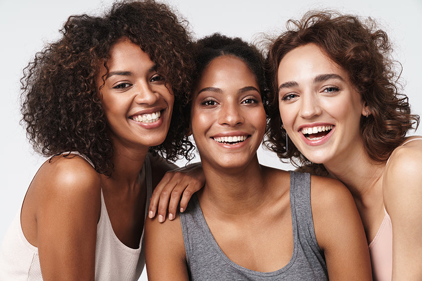 Three smiling women of different ethnicities, displaying three different skin types