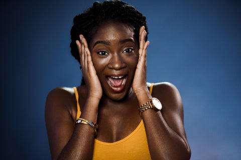African American woman with acne holding her face looking surprised and excited