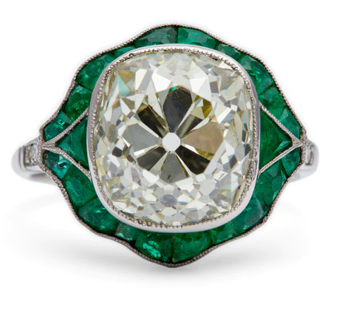 Art deco inspired GIA 6.62 carat old mine cut diamond with 22 calibre cut emeralds surrounding it on a platinum setting