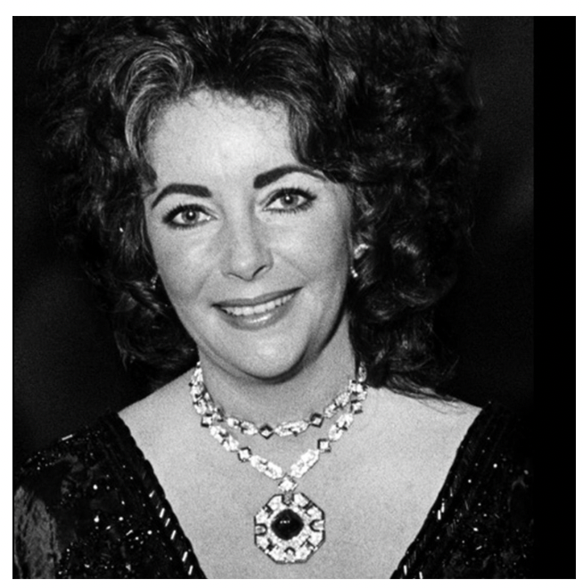 Black and white photograph of a smiling Liz Taylor adorned with the intricate Bulgari sapphire sautoir necklace, its elegance accentuated against her attire and poised demeanor