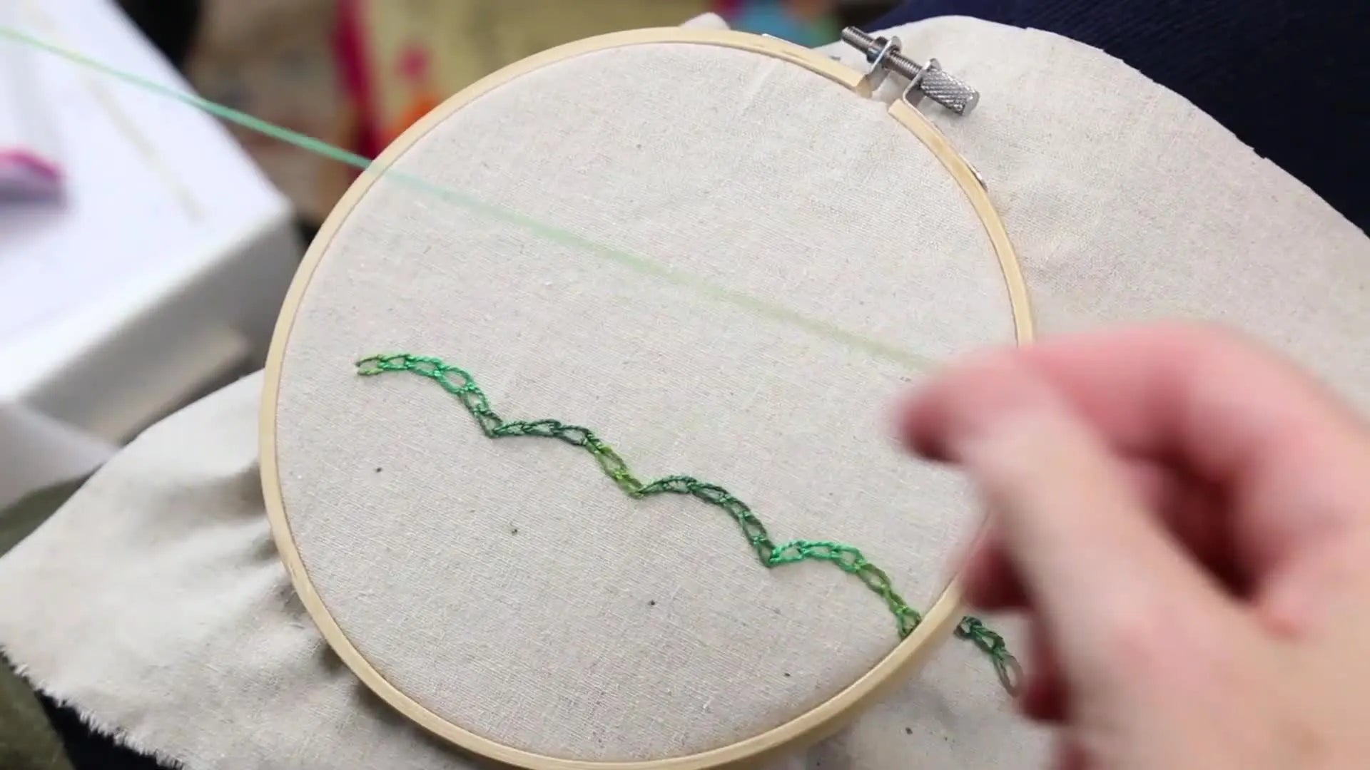 Close-up of fingers threading a needle with variegated pearl cotton.