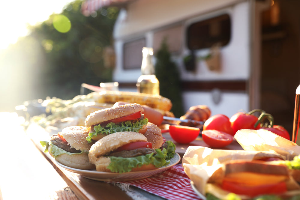 Various burgers, sandwiches and salads on a trestle table in front of a camper trailer