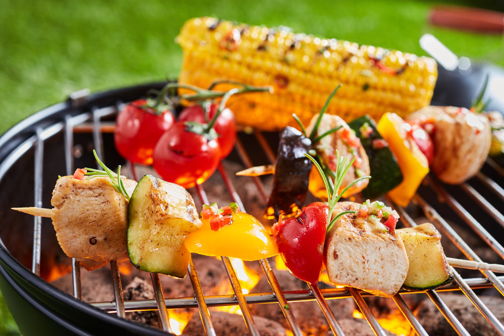 Chicken and vegetable skewers on a BBQ grill with corn cob and cherry tomatoes