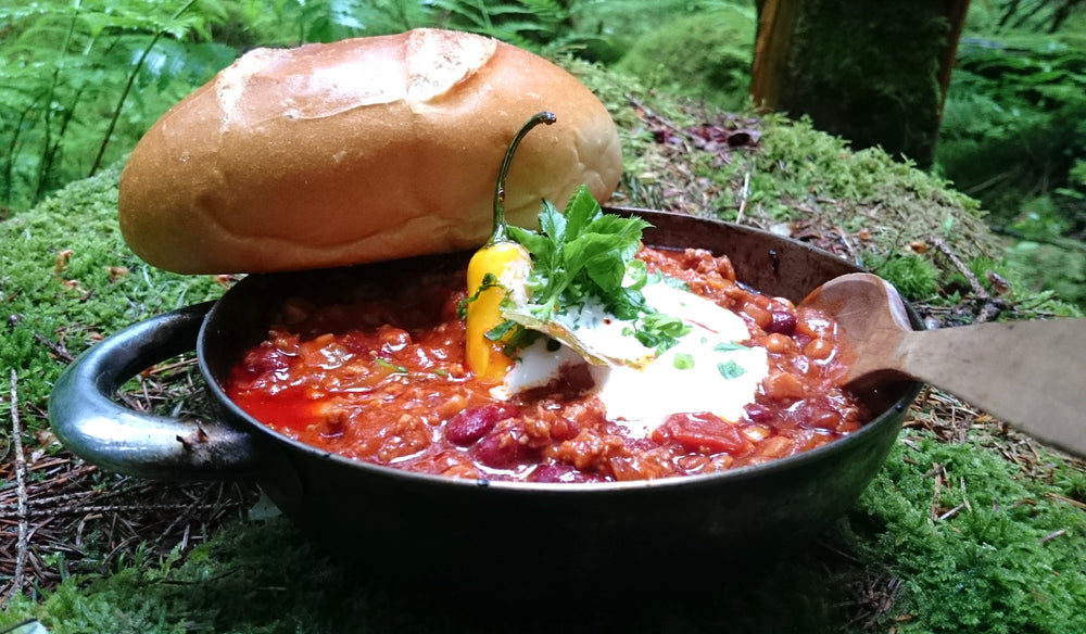 One pot camping stew with loaf of bread and wooden spoon sitting on mossy rock