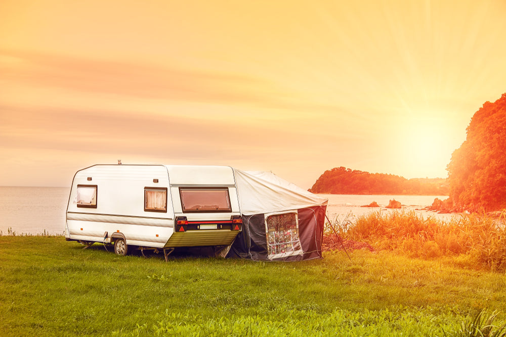 Camper trailer with mesh tent pop-out in front of sunset and mountains