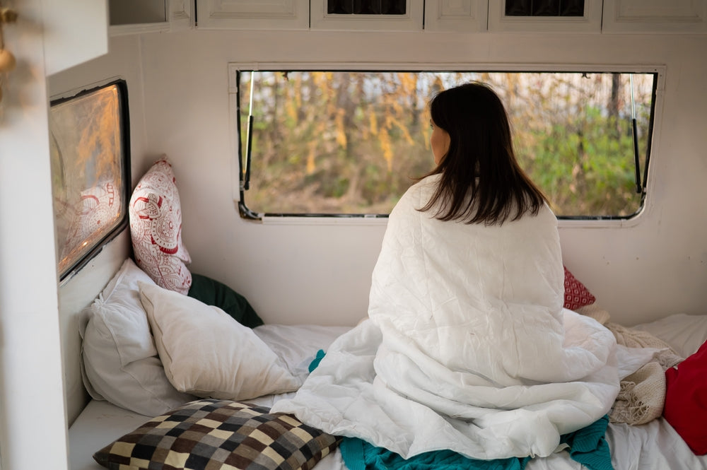 Woman wearing a blanket sitting on her bed in a camper trailer