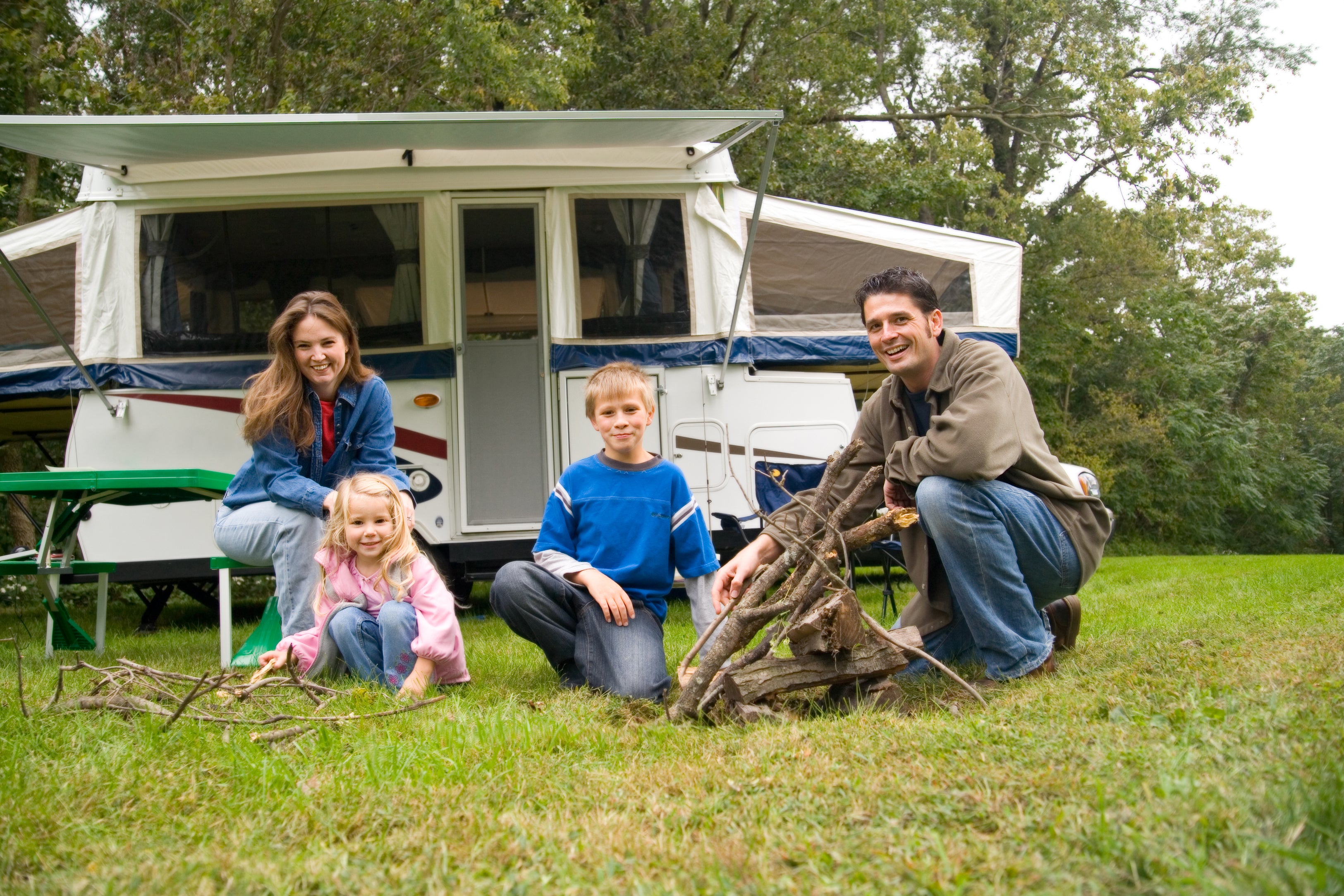 Young family sitting in front of camper trailer at campsite