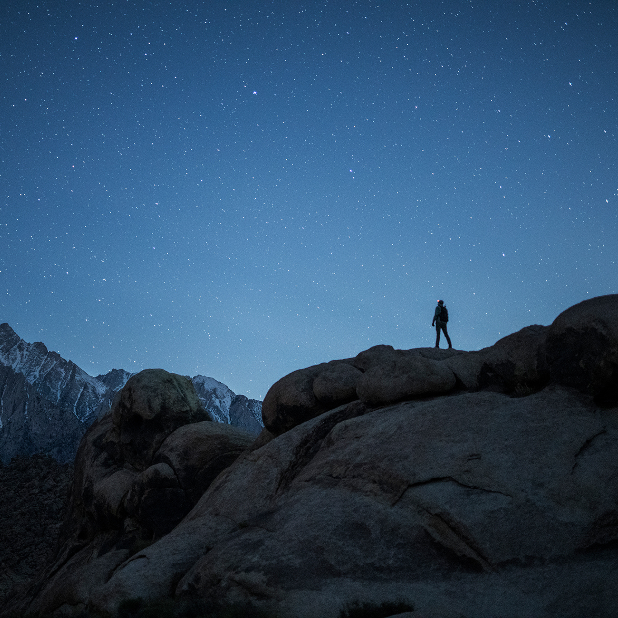 Far away nighttime shot of man on mountains surrounded by a star-filled sky.