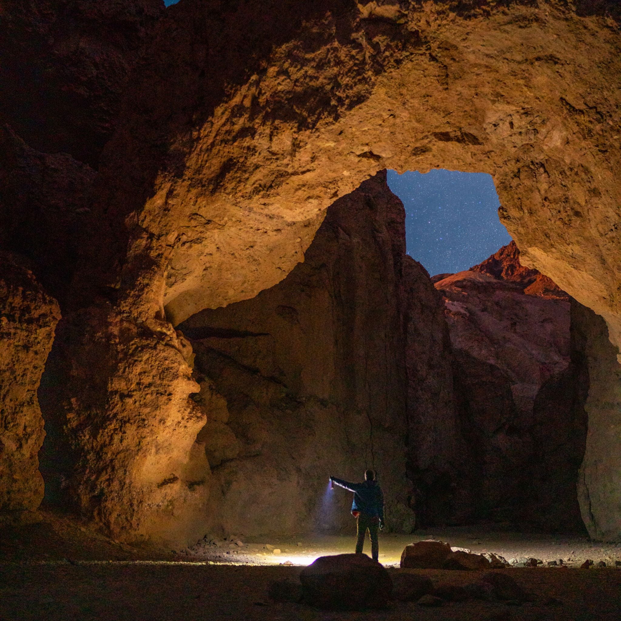 Man standing under arch made of rock holding flashlight