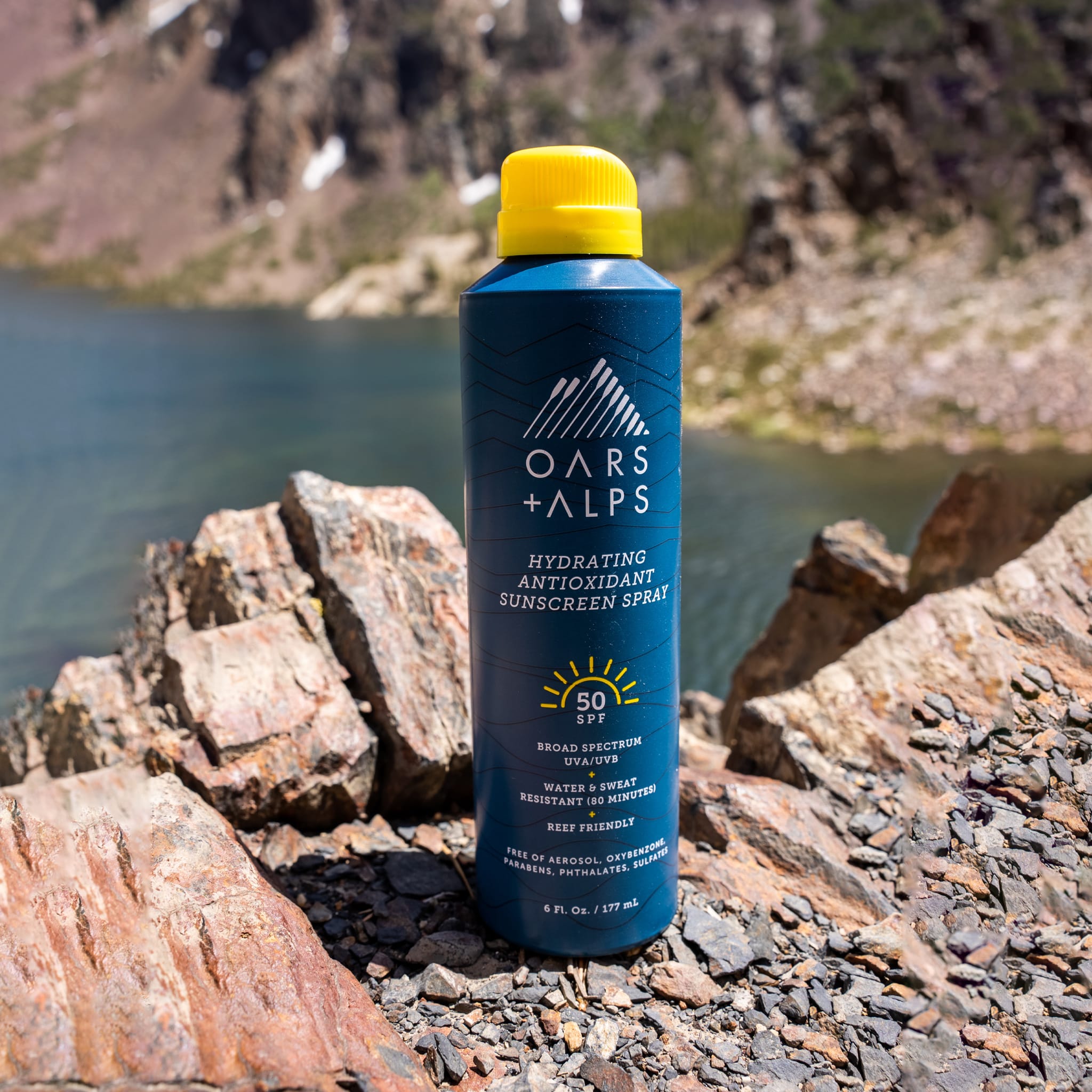 Oars + Alps Hydrating Antioxidant SPF 50 Spray sitting on rock overlooking a body of water 