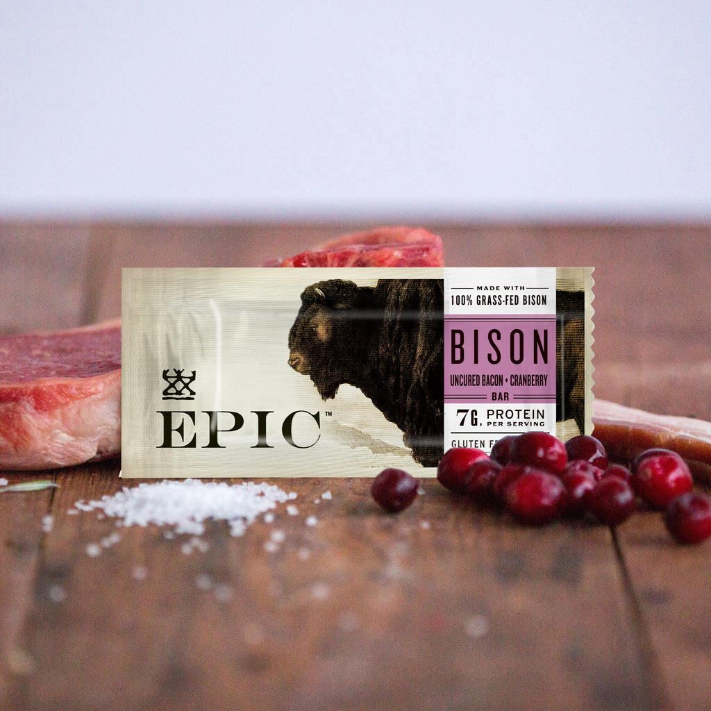 EPIC's Grass-Fed Bison Bacon Cranberry Bar propped up next to bison meat, sea salt, and cranberries on a rustic table.