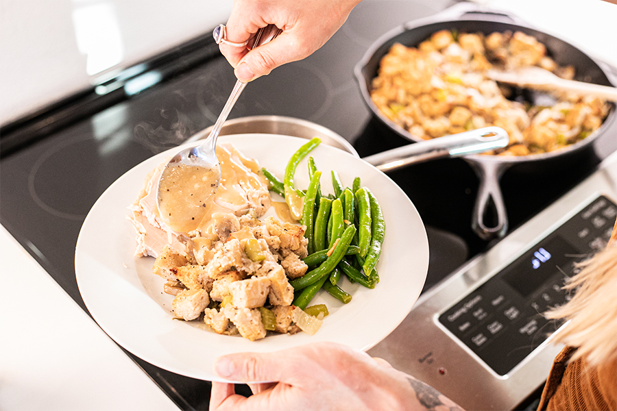 Homemade Chicken Fat Gravy being poured on a plate of turkey, stuffing and green beans.