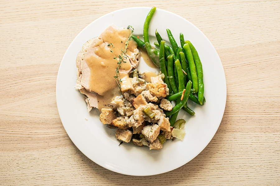 A white plate of turkey and chicken fat gravy, stuffing, and green beans on a wood table.