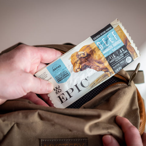 A close up of someone placing an EPIC Beef Barbacoa-Inspired bar in to a backpack.