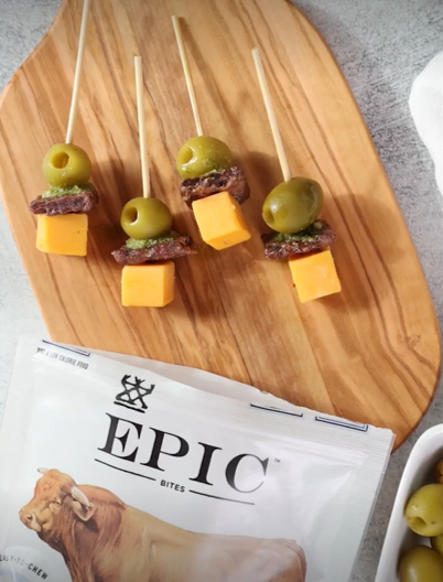 A cutting board with skewers of olives, cheese, and EPIC Beef Sea Salt Pepper Bites on top.