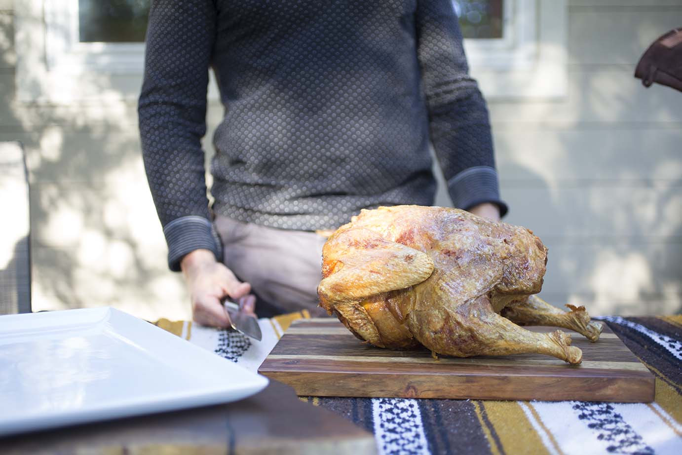 A crispy deep-fried turkey is shown on a wooden table in front of a man with knife 