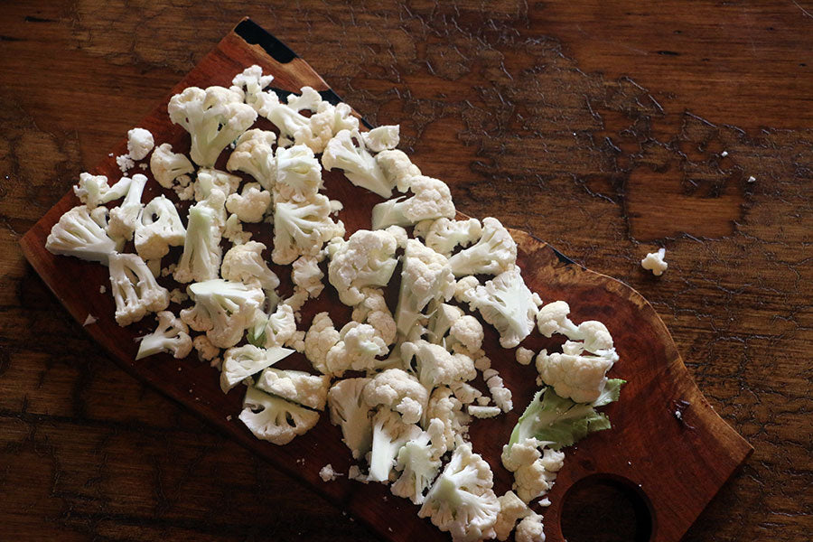 Cauliflower cut in to florets on top of a rustic wood cutting board.