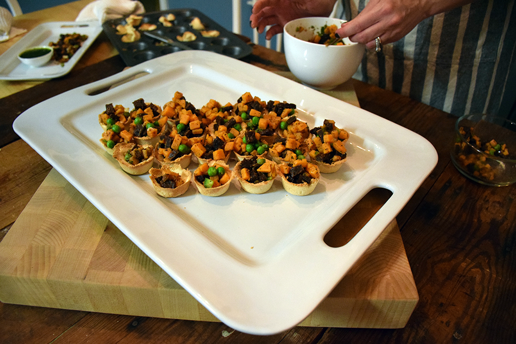 A serving plate loaded with mini paleo samosas as someone fills the samosas.