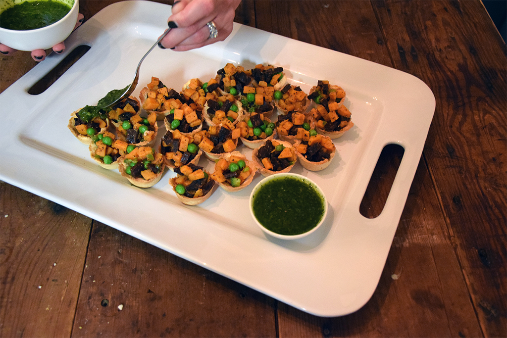 Someone spooning chimichurri sauce on top of the serving tray of samosas.