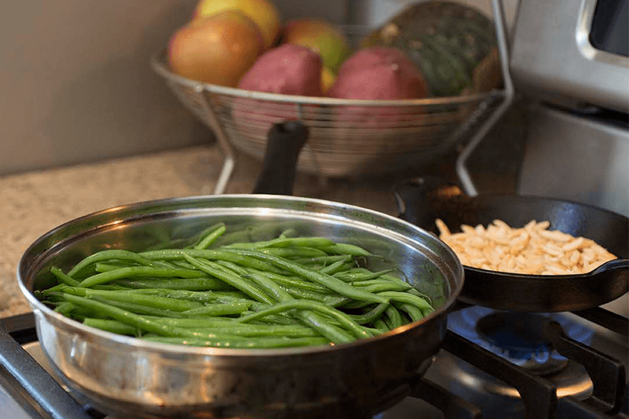 Green beans cooking on stove with bowl of fresh produce in background