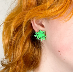 Neon green frog earring on an ear surrounded by orange hair.