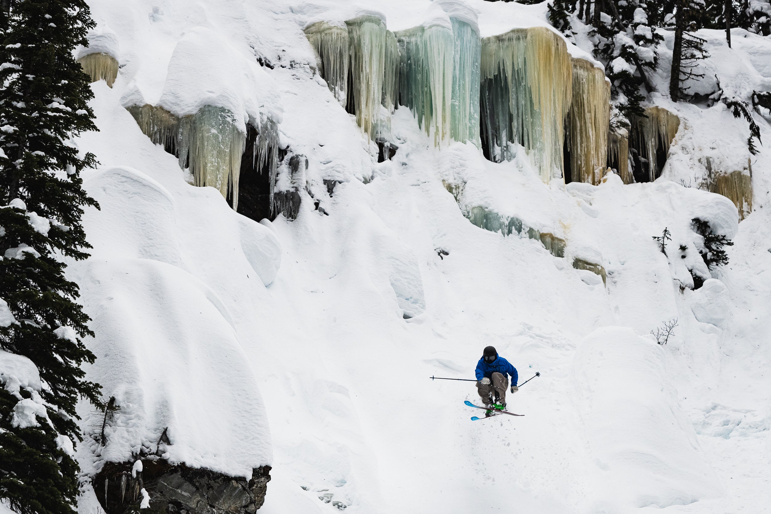 Thor hitting a jump on his Renoun Citadel 106 skis with big ice waterfalls in the background.