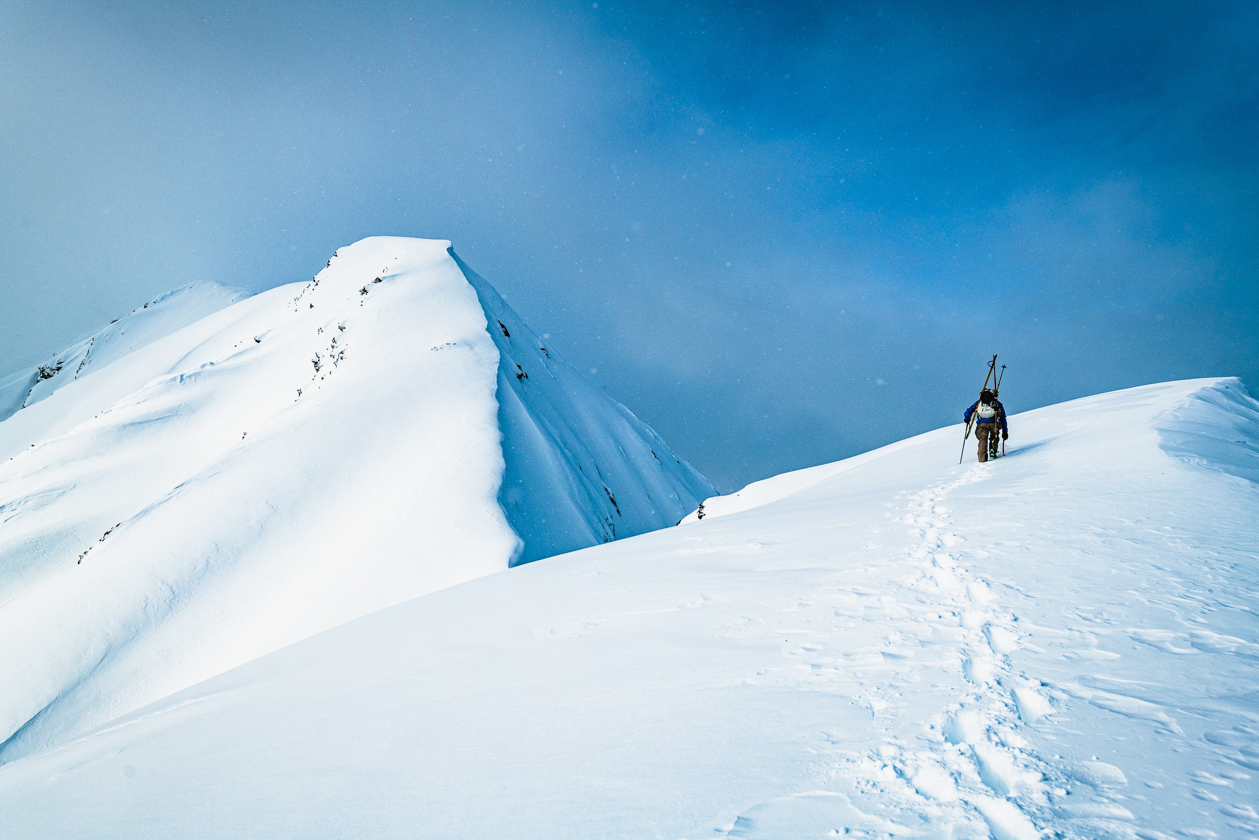 Thor bootpacking out along a snow-covered ridgeline with his skis on his backpack.