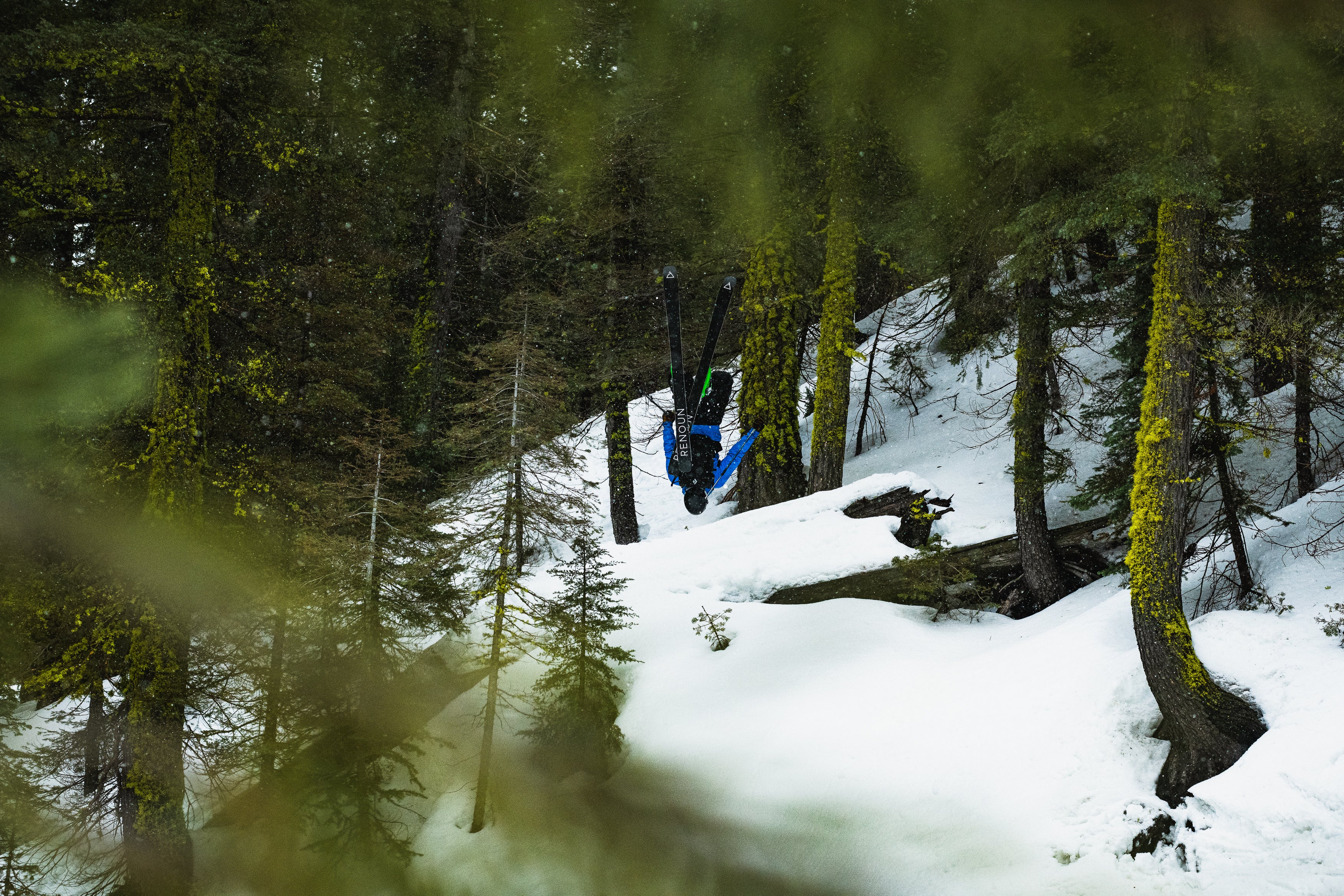 Thor doing a backflip while skiing in the mossy Vermont woods.