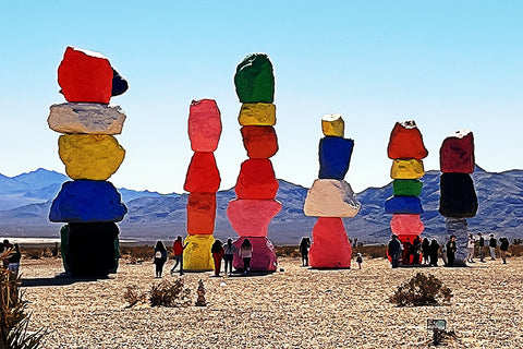 A photo of seven stacks of colored rocks in the desert.