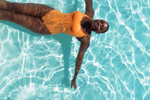Woman smiling and floating in a sunny pool with an orange swimsuit on