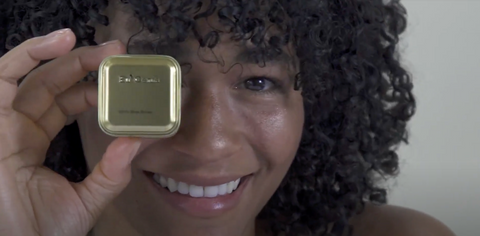 Woman smiling and holding a small gold tin 