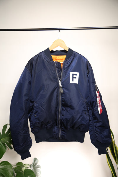 FADER x Alpha MA海军蓝飞行夹克，在衣架上的口袋上有FADER F块