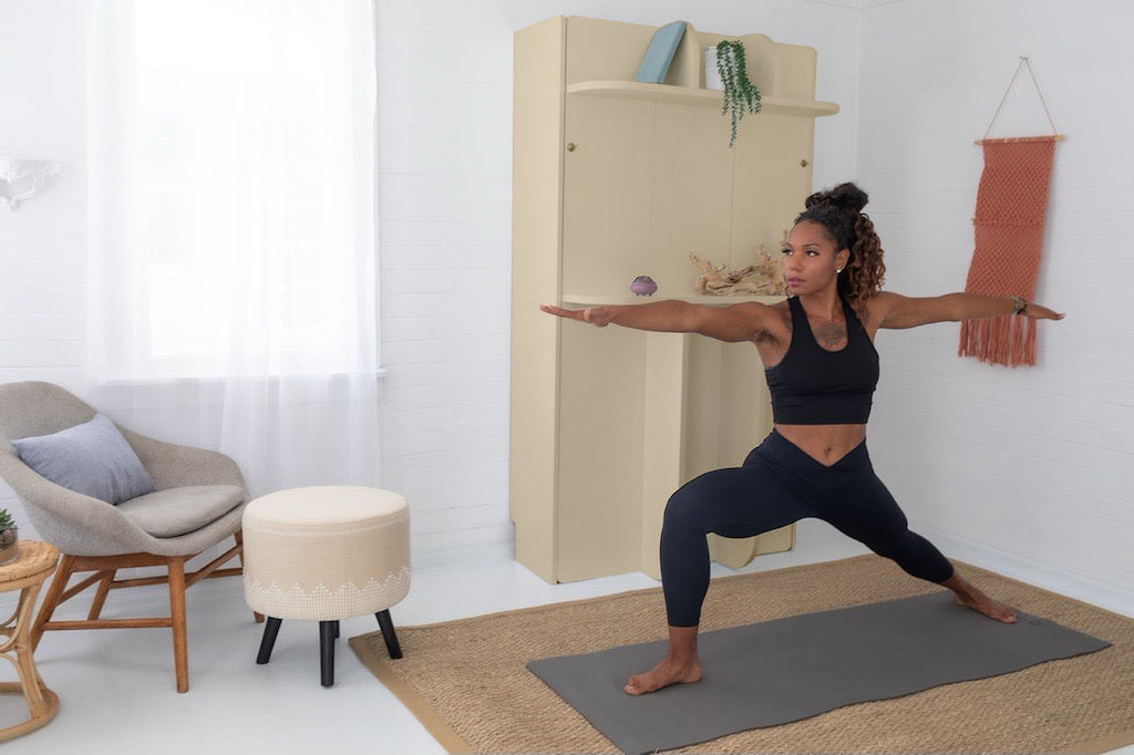 A woman stretching in a home gym with a Lori Bed murphy bed in the background