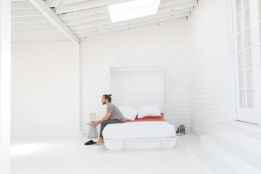 Man in a beautiful minimal studio apartment sitting on a Lori Bed murphy bed