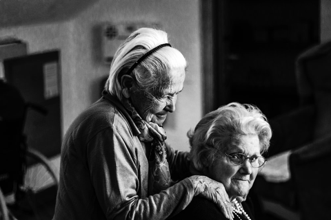 an elderly woman holding onto the shoulder of another elderly woman 