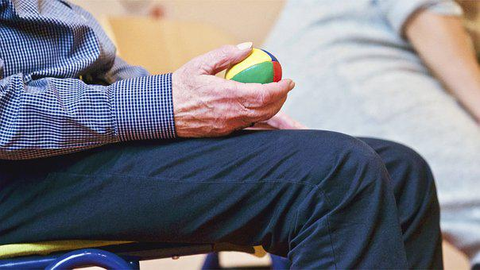an elderly man wearing dark pants and holding a colourful ball