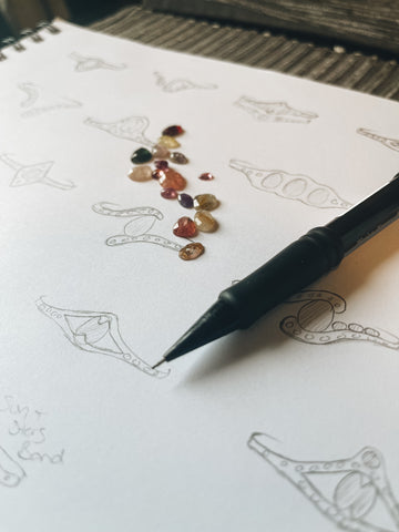 Drawings of different ring designs and a pile of rustic looking gemstones.
