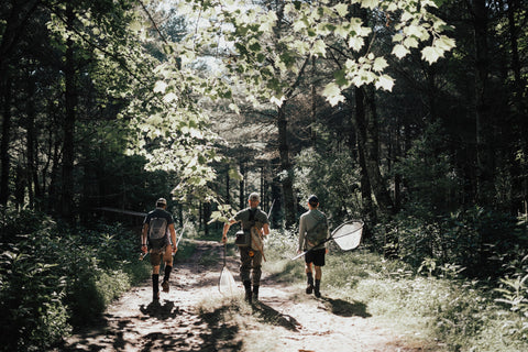 three men walking walking in the woods with their fly rods