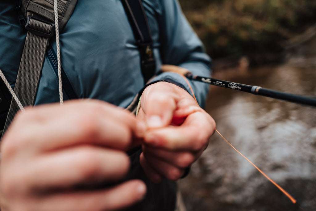 In this image, from Moonshine Rods, an anger is tying a fly on the end of his rod.