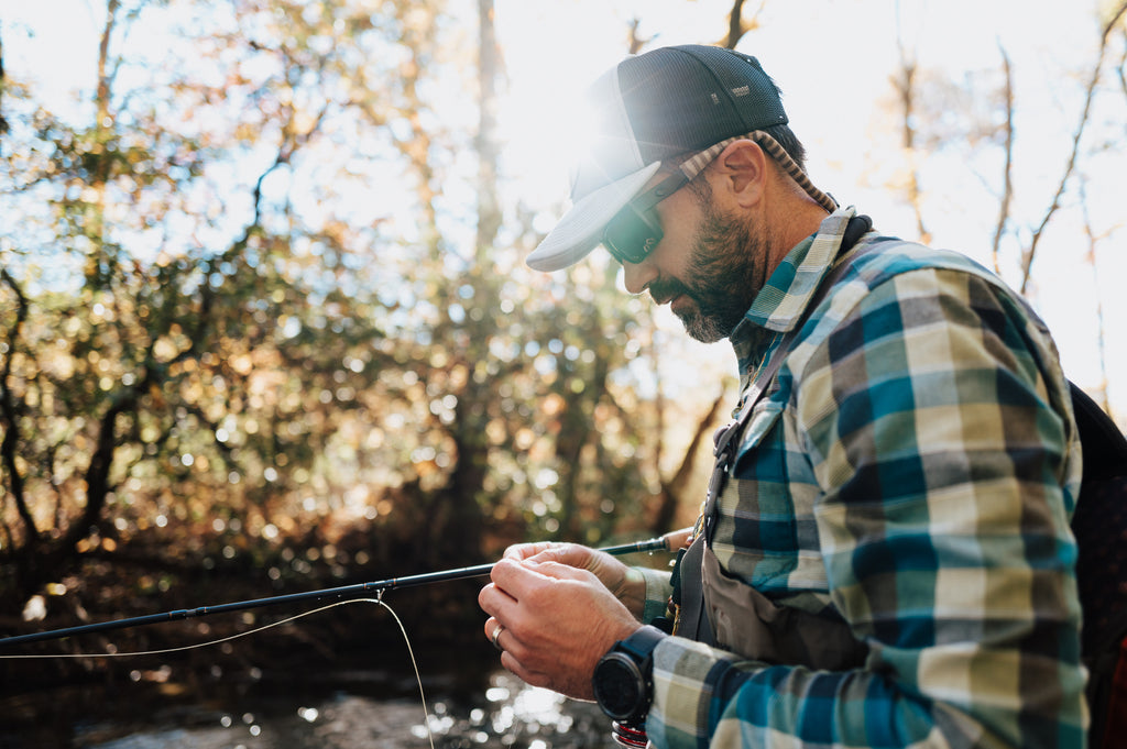 In this image, from Moonshine Rods, an angler is tying a fly on his line.