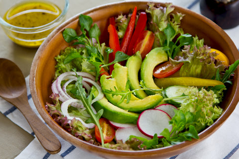 avocado and greens salad in a wooden bowl with a side of dressing