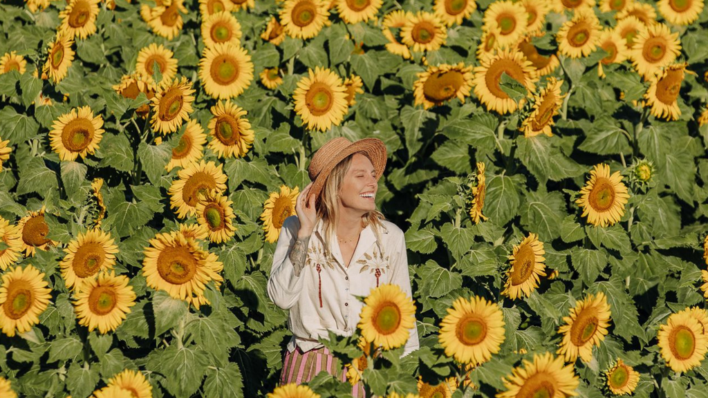 Sweet blonde girl in a straw hat stands in the middle of a field of sunflowers