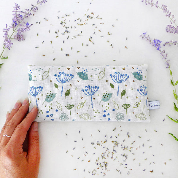 A floral printed lavender eye pillow surrounded by a sprinkling of lavender and dried lavender stems.