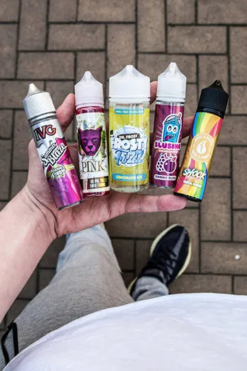 Someone holding five bottles of e-liquid in an open palm over a brick road.