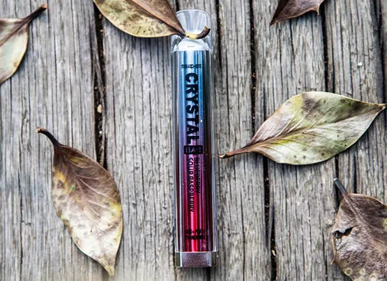 A SKE Crystal Bar disposable vape device laying down on a wooden table, with leafs surrounding.